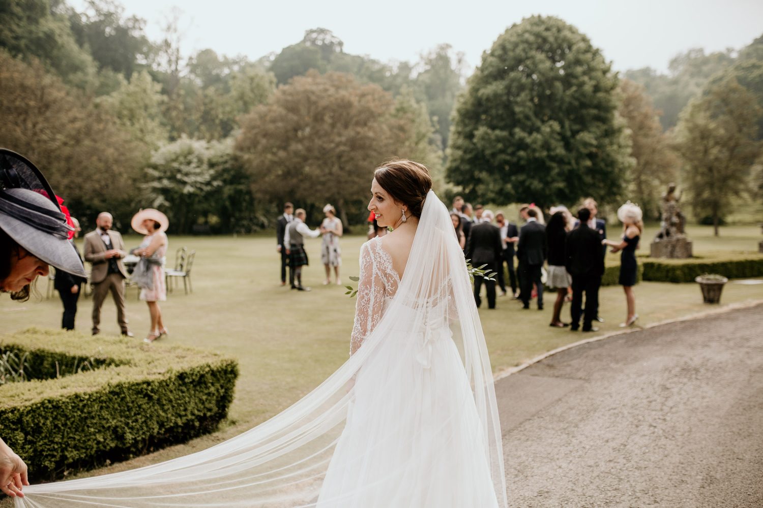 luxury manor house hotel wedding photos of the bride looking over her shoulder with her train behind her and the wedding guests in the background