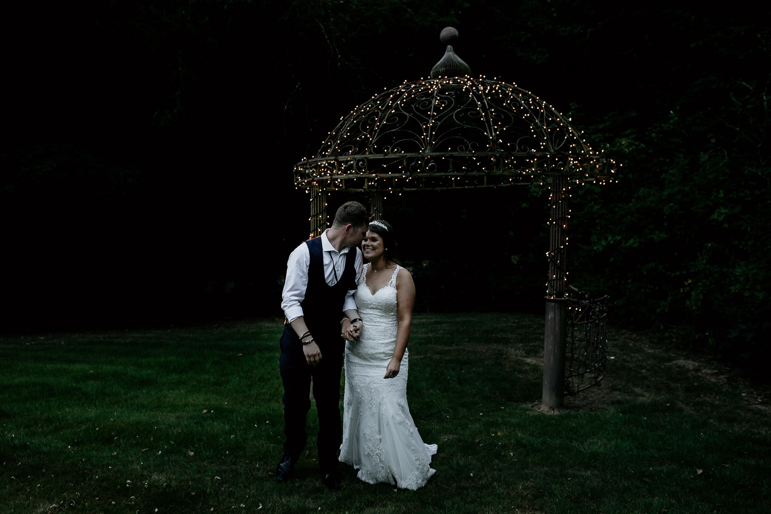 photo of groom looking back at bride outdoors near fairy lights