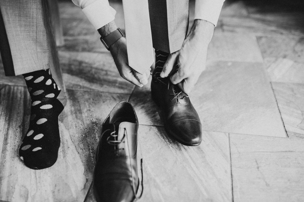 black and white close up of groom in odd socks doing up shoes on morning of wedding