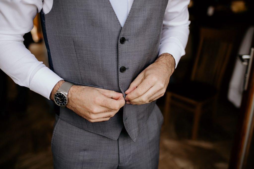 close up of groom in white shirt, grey trousers and luxury watch doing up grey waistcoat