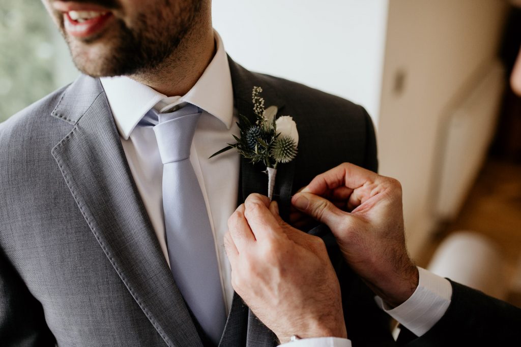 close up of grooms grey suit with light blue tie and green and white buttonhole