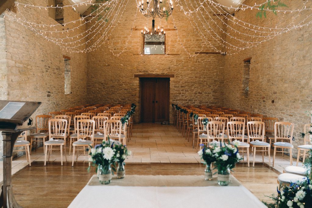 luxurious barn conversion wedding venue vintage wooden chairs decorated with flowers in vases, beams and fairy lights