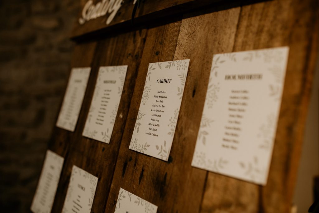 close up of personalised wedding decorations rustic wooden board decorated with green foliage displaying table seating plans