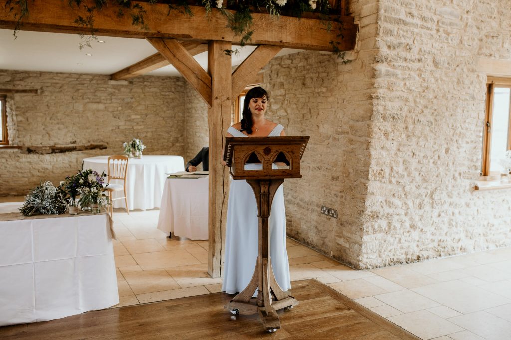 bridesmaid in blue dress gives wedding speech in luxurious barn conversion beamed wedding venue
