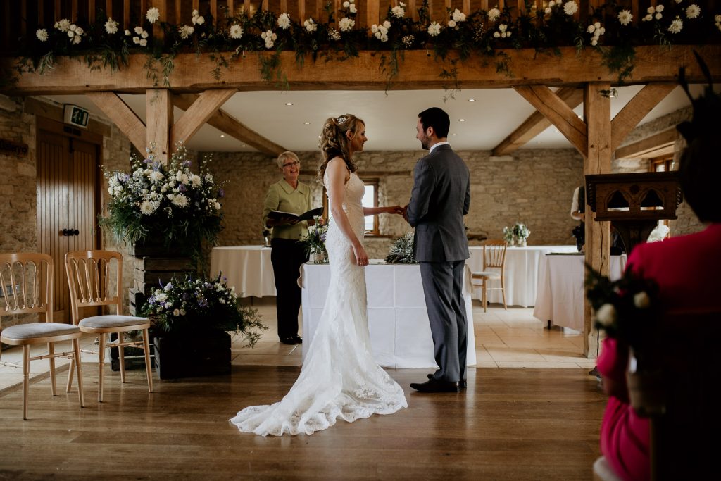 bride and groom stand hand it hand at the alter in luxurious beamed barn conversion wedding venue