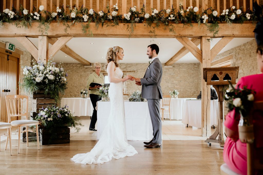 bride and groom stand hand it hand at the alter in luxurious beamed barn conversion wedding venue