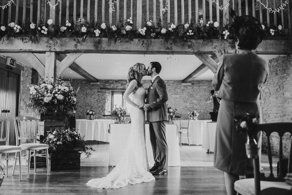black and shite photo of bride and groom kissing at the alter in luxurious beamed barn conversion wedding venue