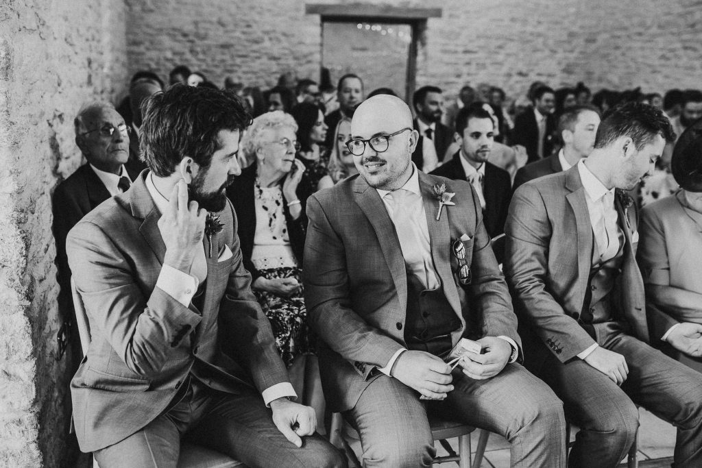 black and white photo of groomsmen and wedding guests seated in luxurious beamed barn conversion wedding venue