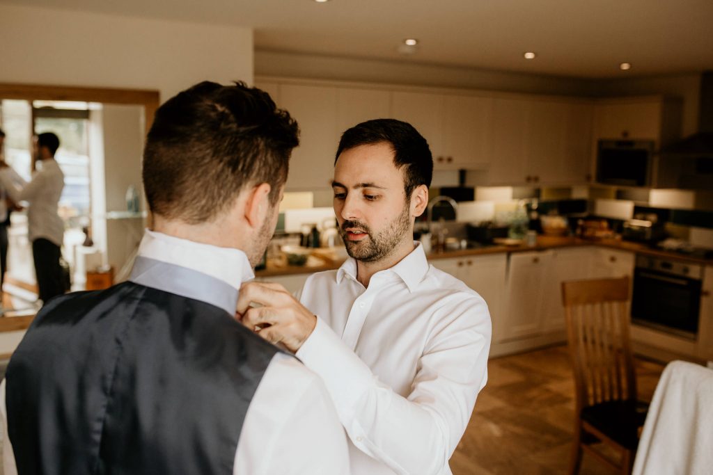 Groom is helped with his tie by best man on the morning of the wedding