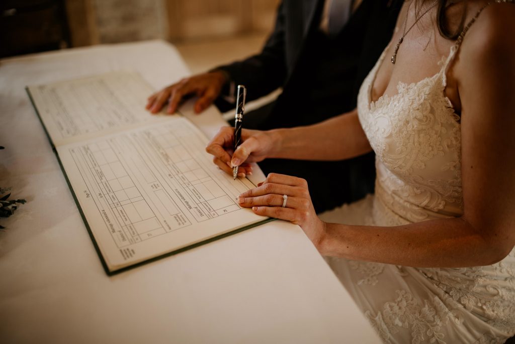 close up of bride and groom signing marriage register in luxurious beamed barn conversion wedding venue