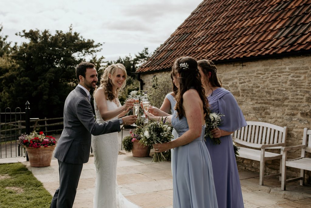 bride, groom and bridesmaids celebrate with champagne outside of luxurious beamed barn conversion wedding venue