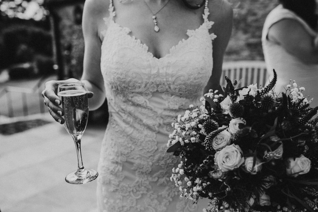 black and white close up of bride in embroidered wedding gown holding luxurious floral bouquet and champagne glass