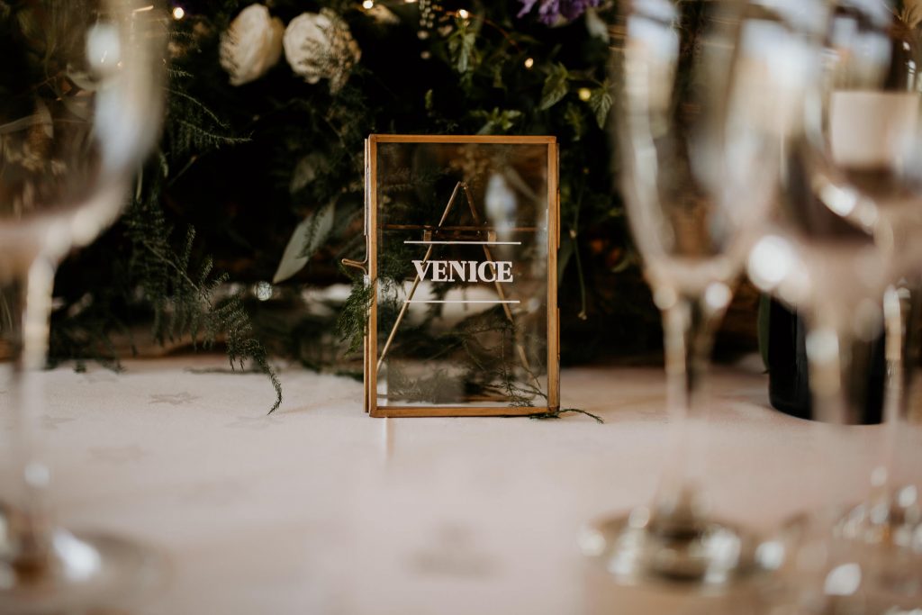personalised wedding decorations table with glassware, glass venice sign, white roses and dark green foliage