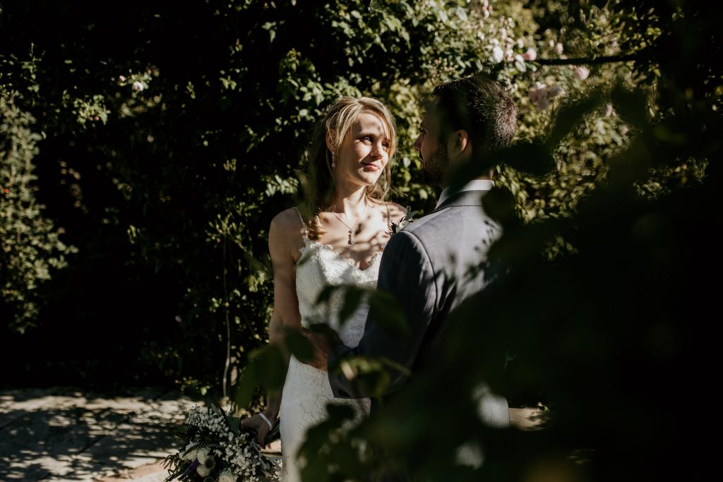 bride and groom stand hand in hand surrounded by rich green foliage