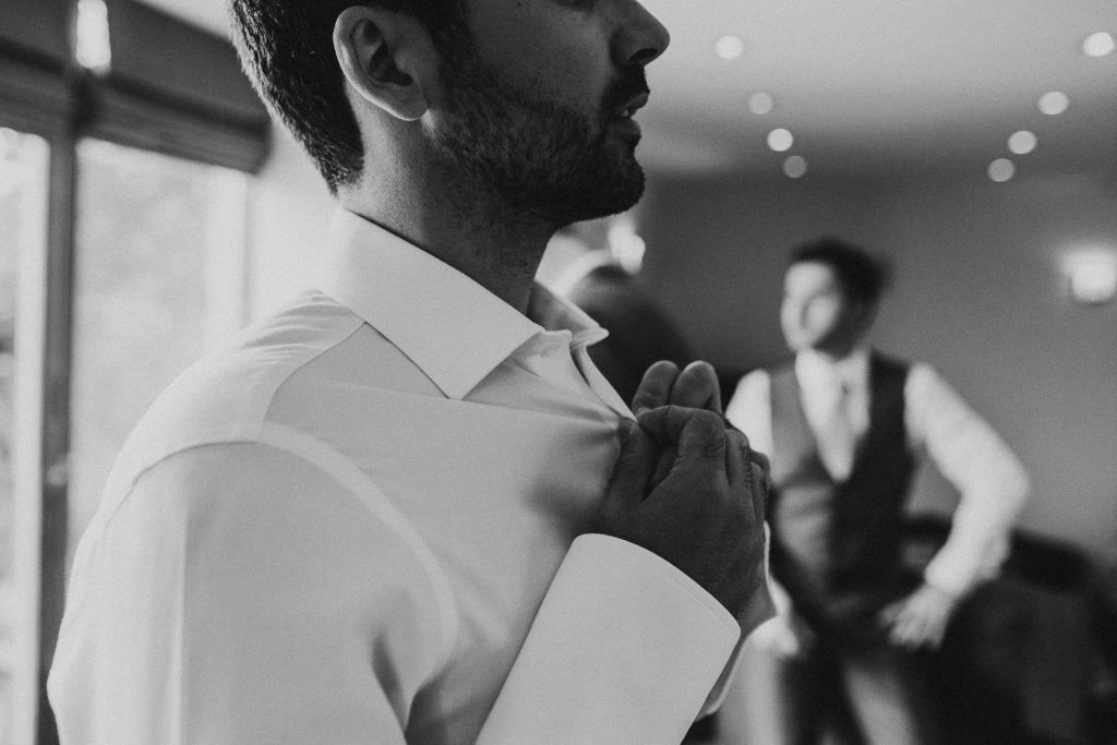 black and white close up photo of groom doing up his shirt on the morning of the wedding
