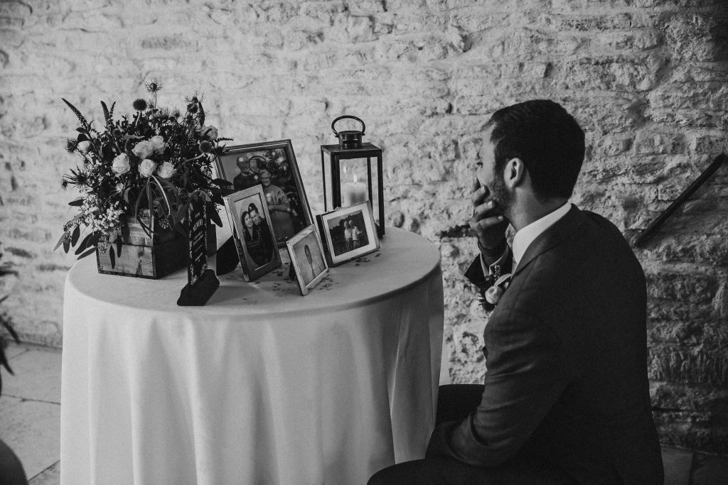 sentimental black and white photo of groom looking at photos of family members on in memory of table
