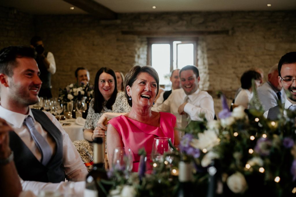 fun and relaxed photo of wedding guests smiling and laughing along to speeches in luxury barn conversion reception venue kingscote barn