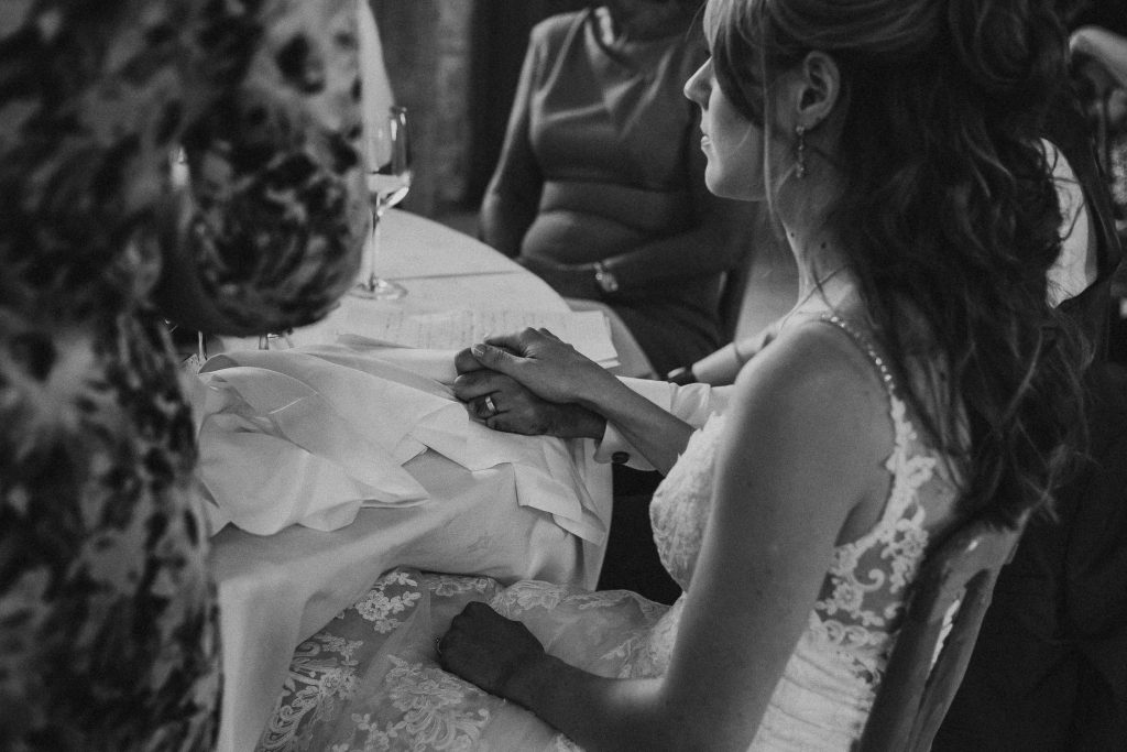 black and white photo showing bride and groom holding hands seated during wedding speeches