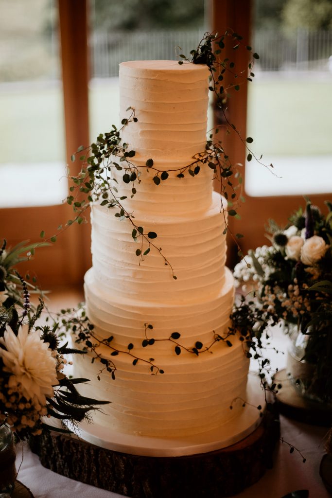 Luxurious and minimalistic 5 tiered wedding cake decorated in simple and chic white icing with delicate dark green foliage