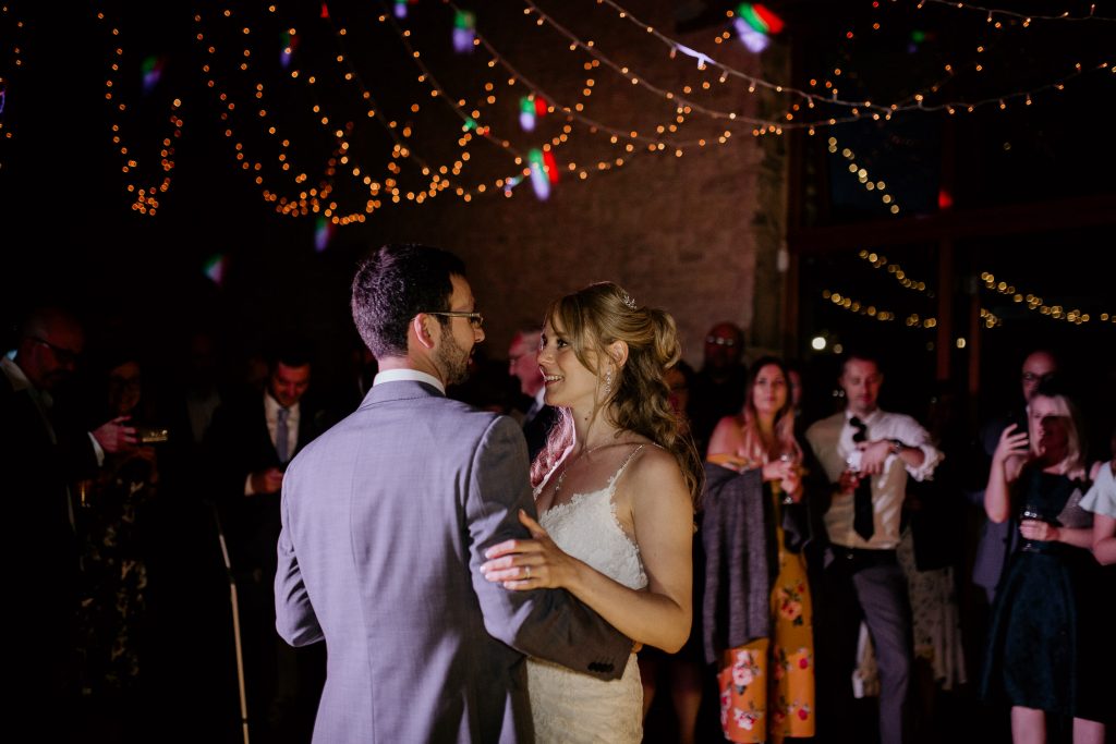 bride and groom dance their first dance on empty dance floor as guests watch on