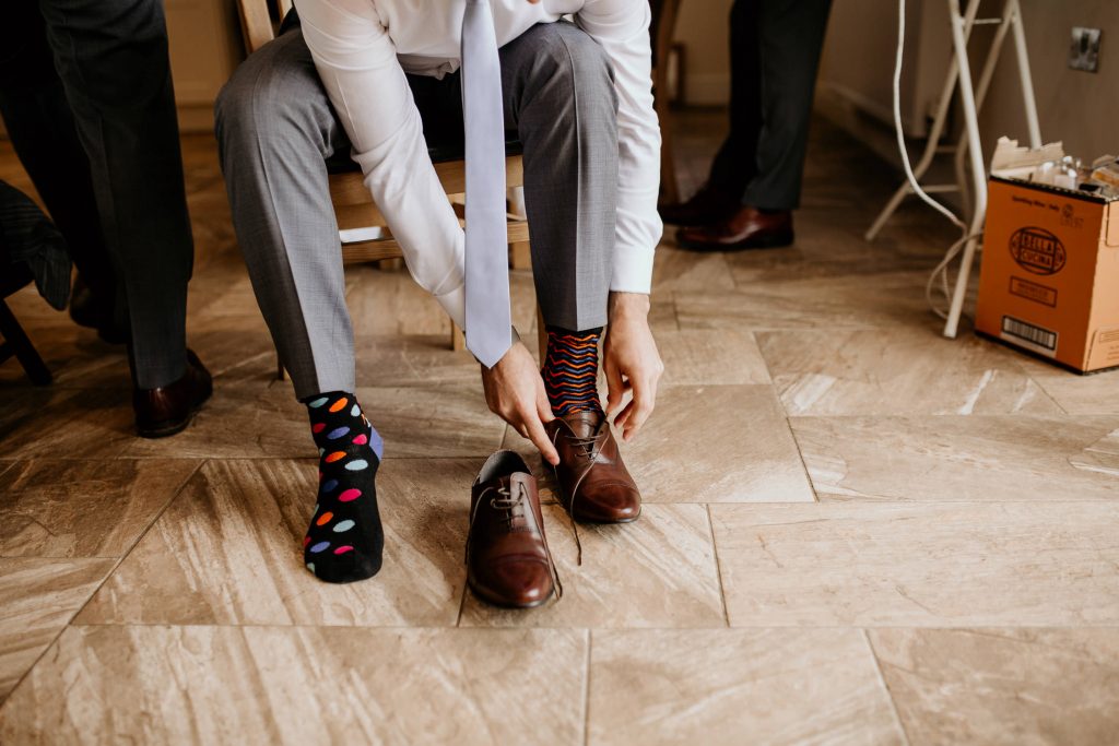 close up of groom in brightly coloured odd socks doing up shoes on morning of wedding