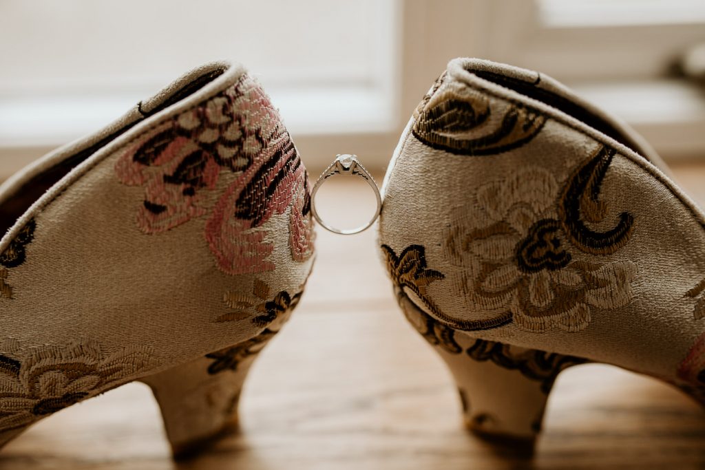 artsy photo showing engagement ring balanced between unusual quirky wedding shoes