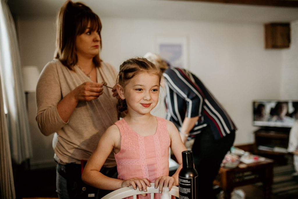 woman does hair of young smiling bridesmaid in pick dress