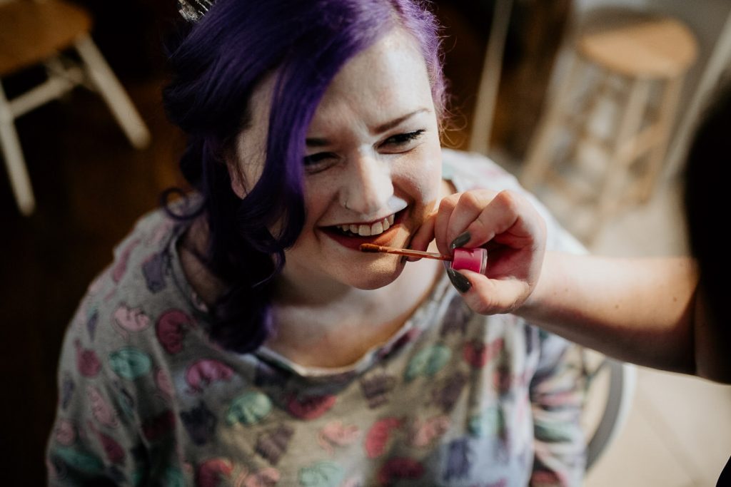 fun photo of quirky alternative bride smiling whilst having her wedding make up applied