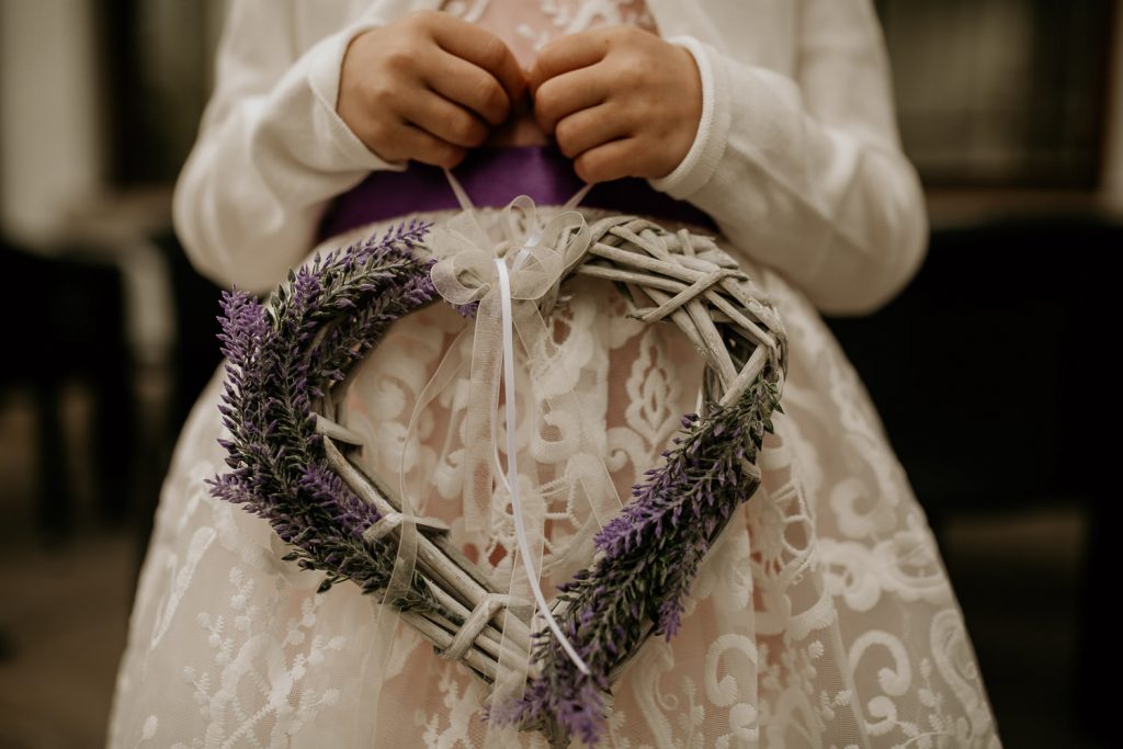 close up on young bridesmaid holding heart made of wicker decorated with white ribbon and lavender