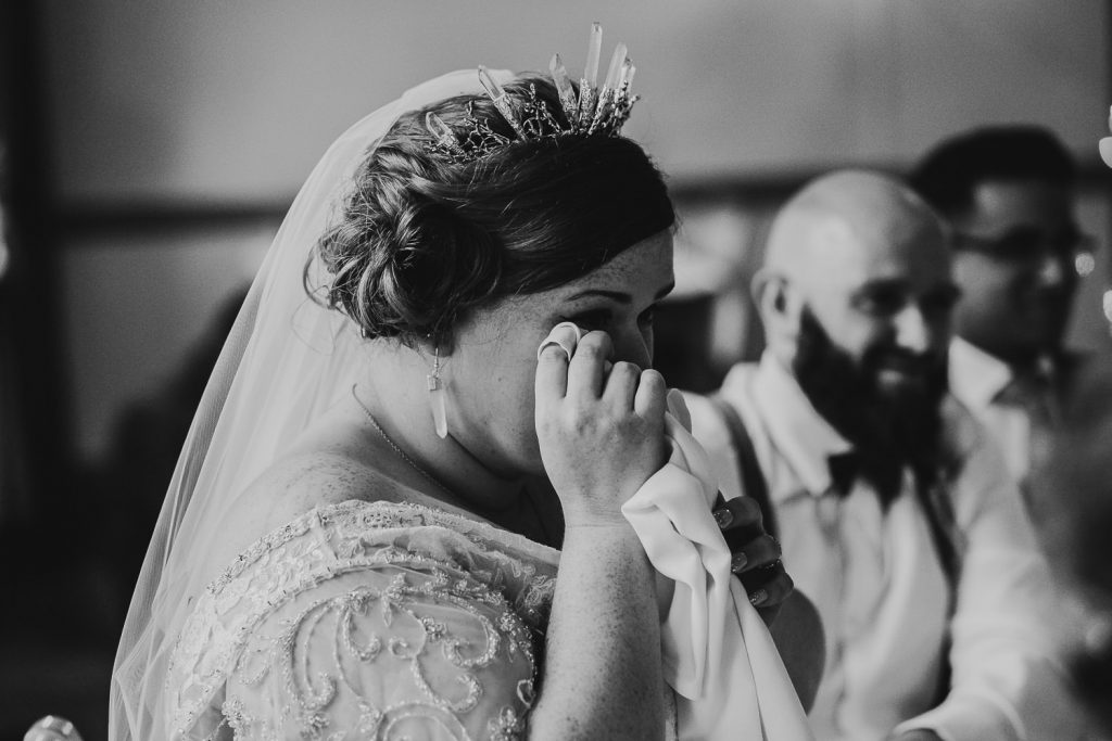 black and white emotional photo of bride crying during speeches and groom smiling in background