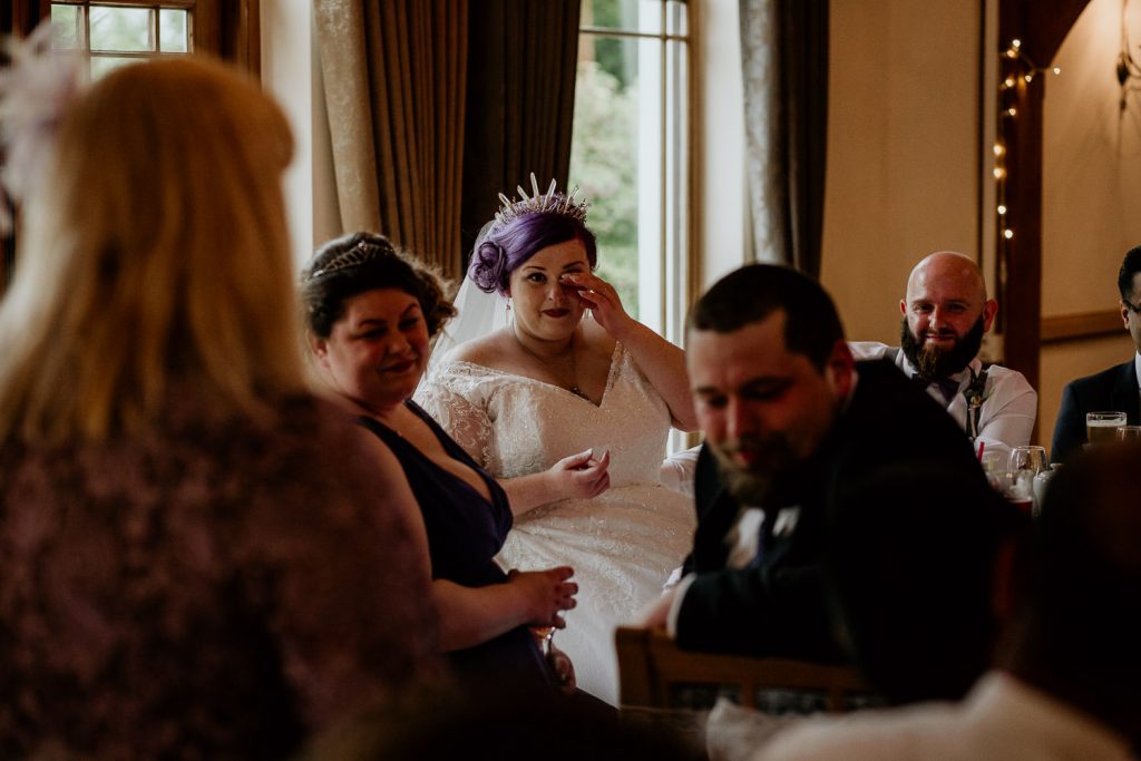 emotional photo of bride crying during speeches and groom and other bridal party smiling around her