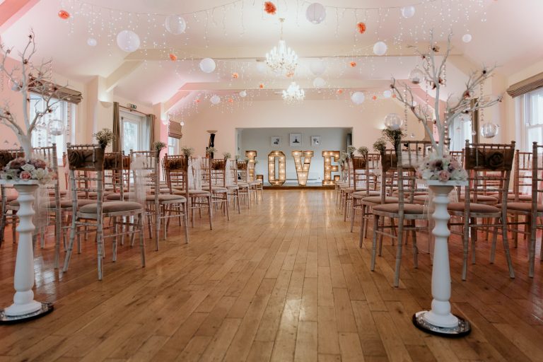 romantic and fun ceremony venue decorated with pink and white vintage chairs fairly lights hanging paper balls and large light up LOVE sign