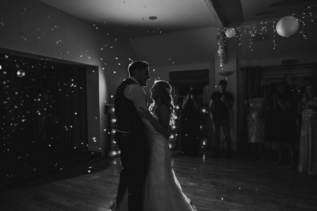 black and wite poto of bride and groom dancing on empty dance floor with confetti falling around them
