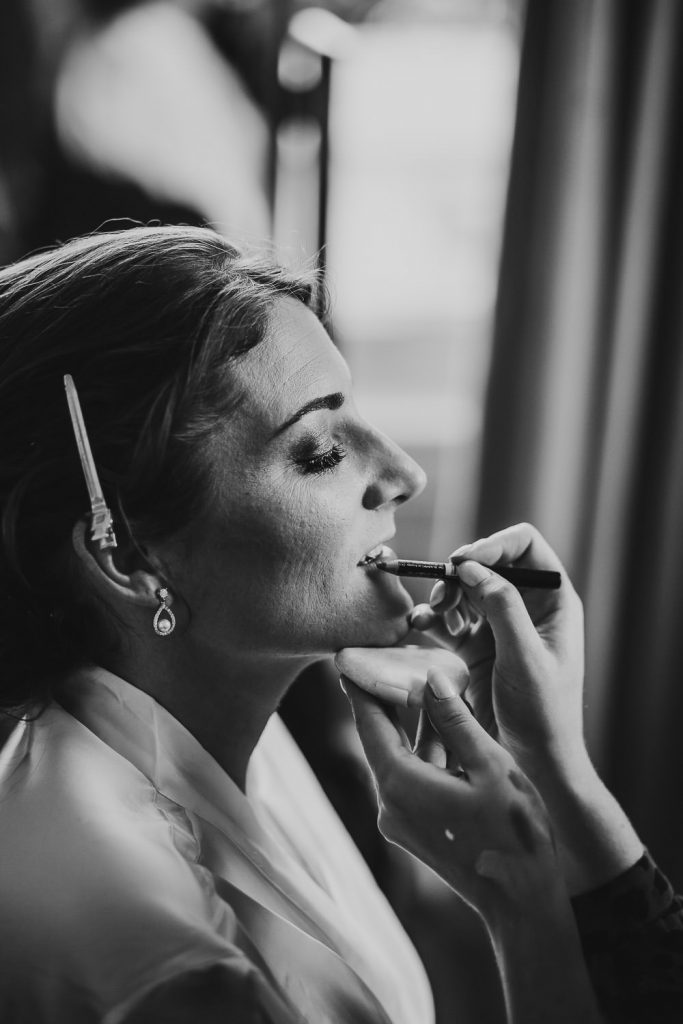 black and white close up of bride in white dressing gown having her make up done on the morning of the wedding