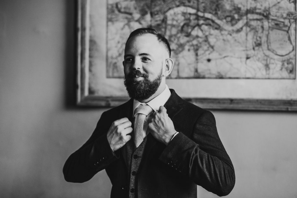 black and white photo of groom putting on his wedding jacket