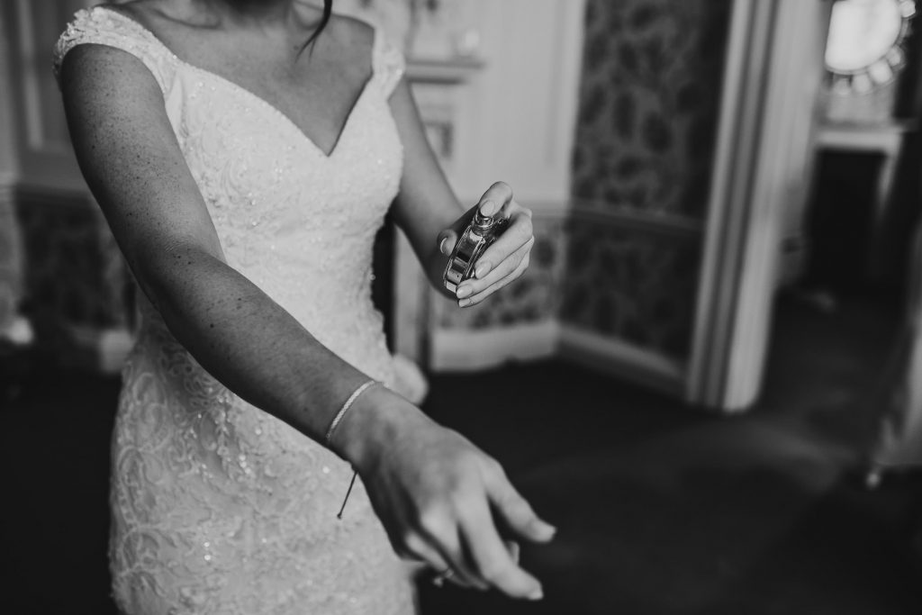 black and white photo of bride in white jewelled wedding gown applying perfume