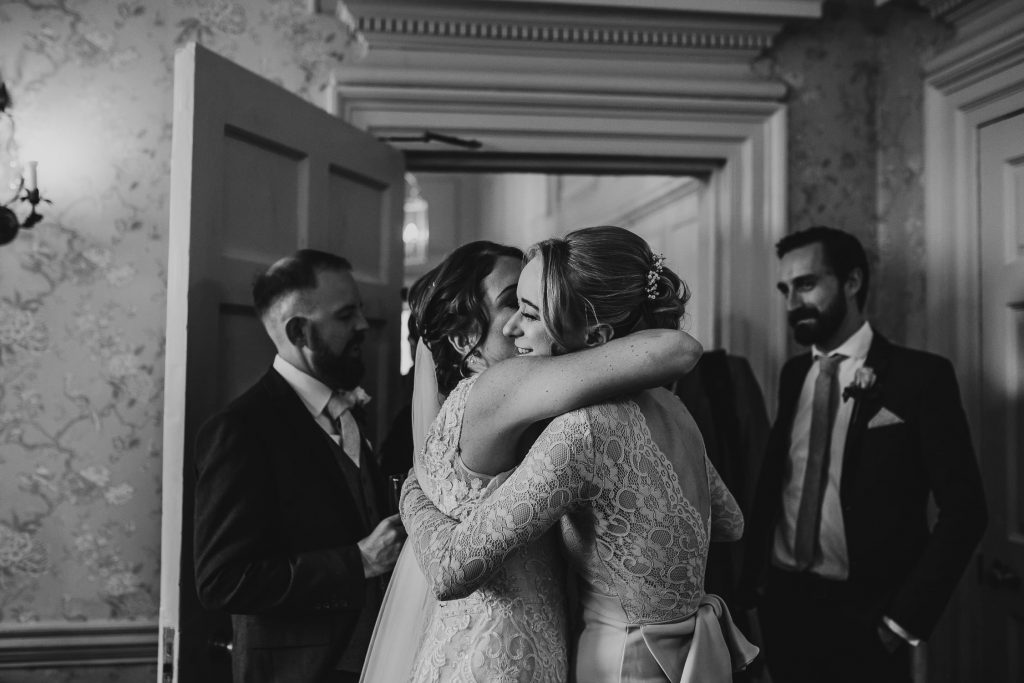 black and white photo of bride and groom greeting wedding guests bride embraces bridesmaid