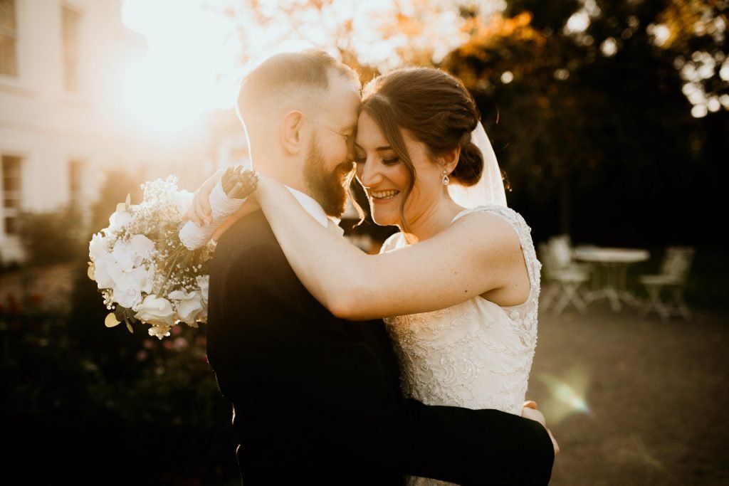 golden hour photo of bride and groom laughing and hugging in front of the setting sun