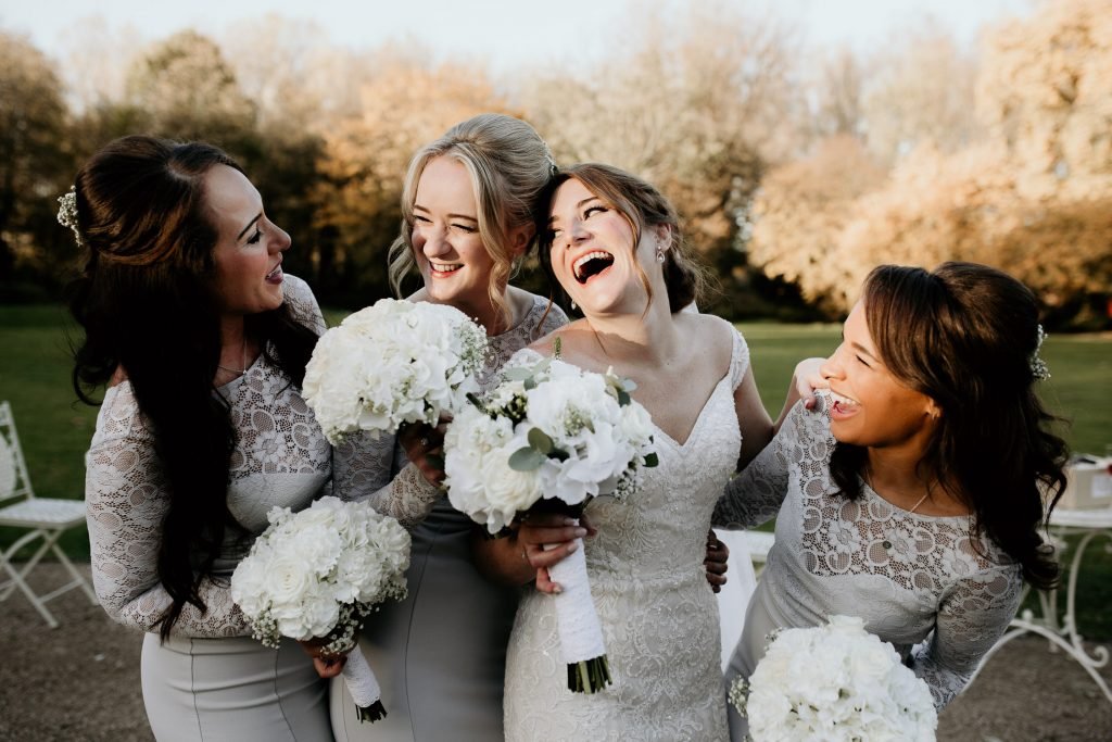 fun and relaxed photo of bride and bridesmaids laughing outside of wedding venue in the sunshine