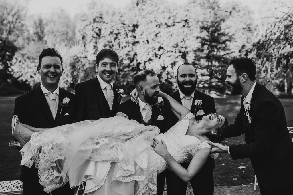 black and white photo of groom and groomsmen carrying laughing bride