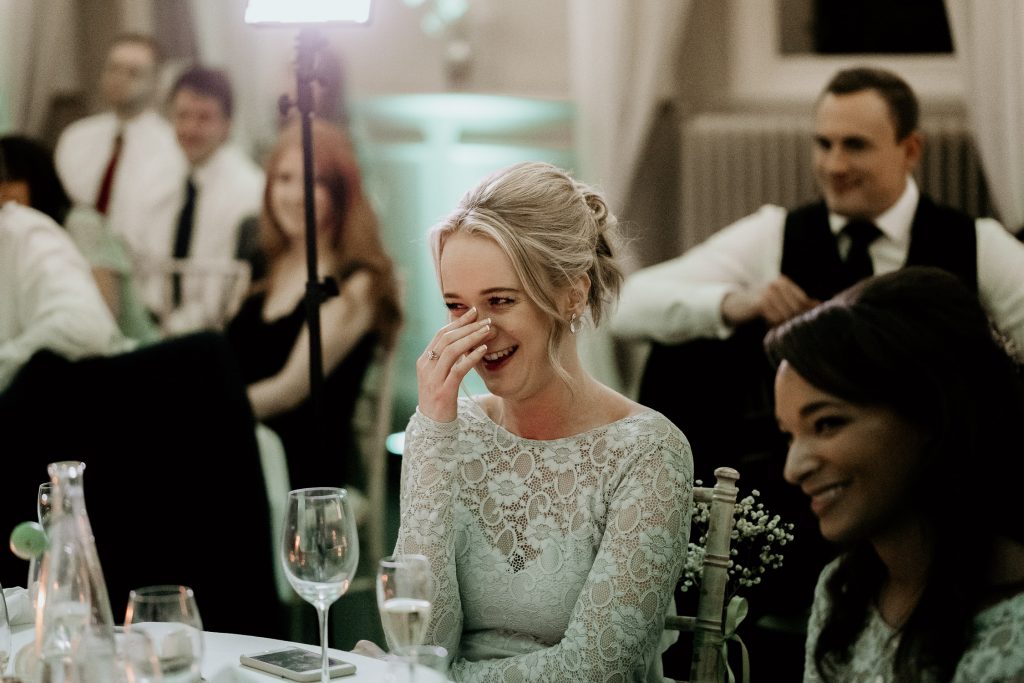 photo of bridesmaid in light floral lace dress laughing at wedding speeches