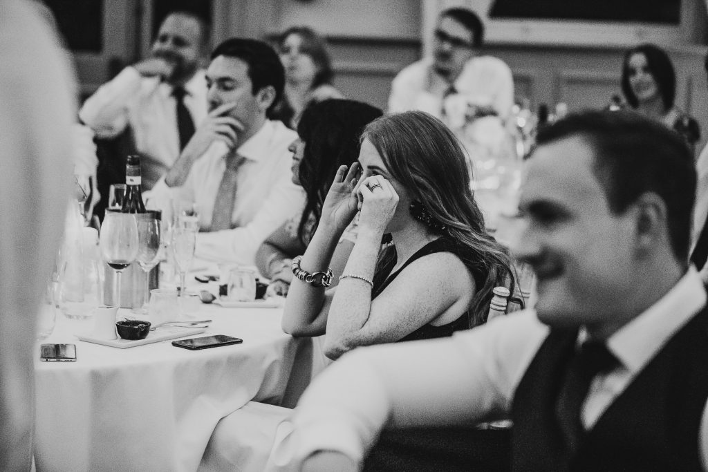 emotional black and white photo of wedding guests laughing and crying along to the speeches