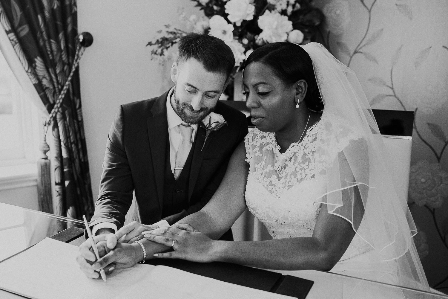 black and white photo of smiling bride and groom sign their wedding register