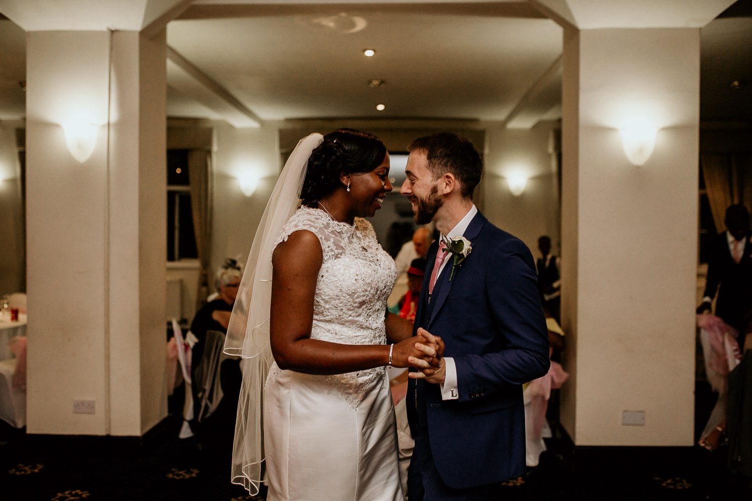 bride and groom smiling at each other and dancing with guests sitting in the background