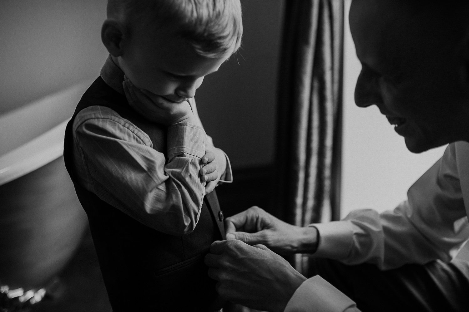 black and white photo of groom helping young boy with is suit before the wedding