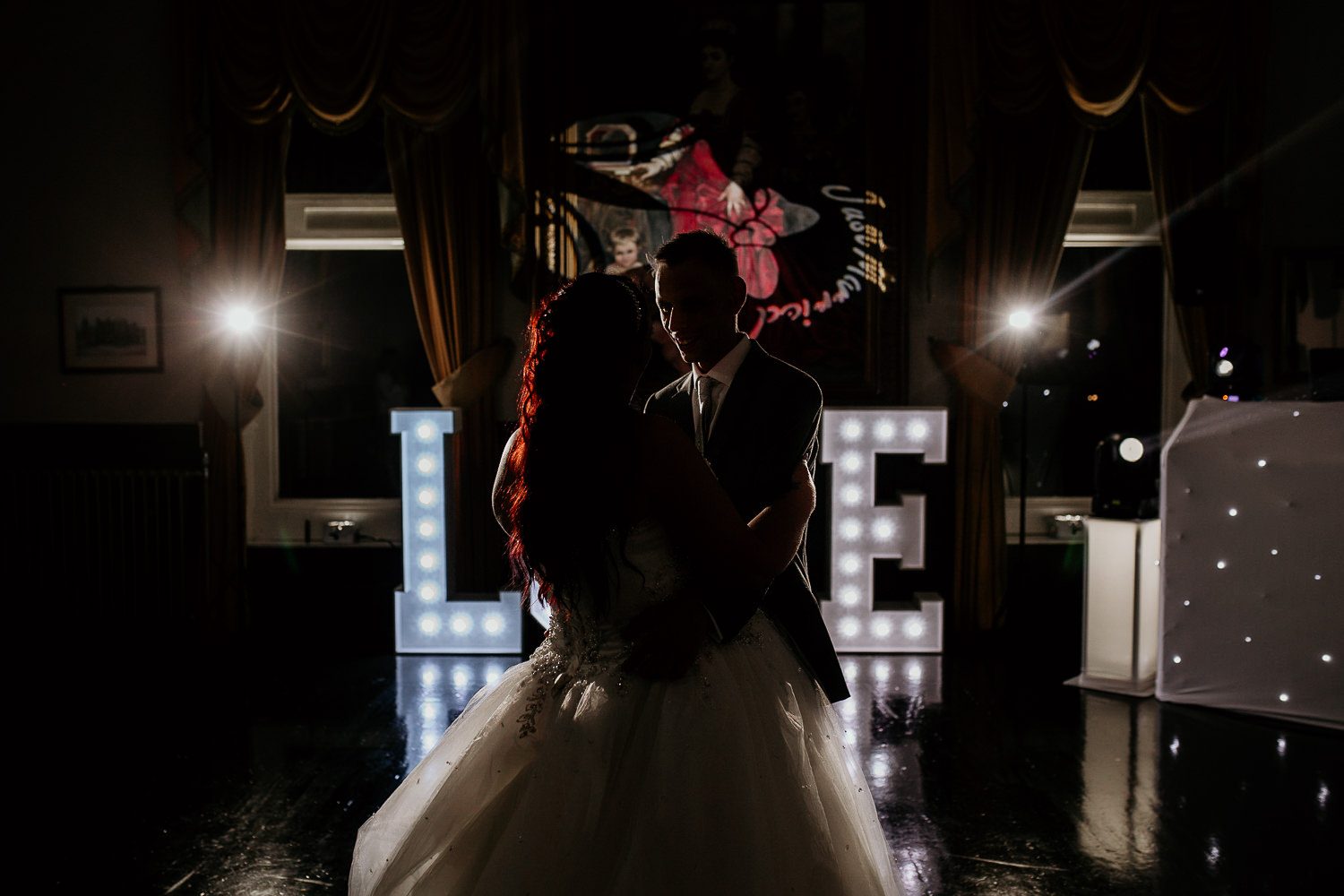 bride and groom in silhouette dancing in front of light up LOVE sign