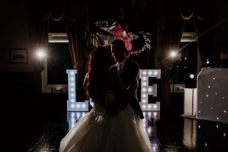 bride and groom in silhouette dancing in front of light up LOVE sign