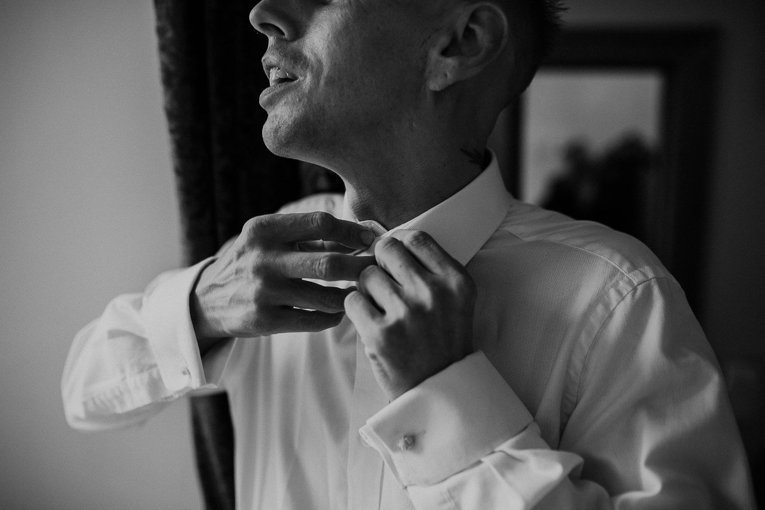black and white close up of groom doing up his shirt before the wedding