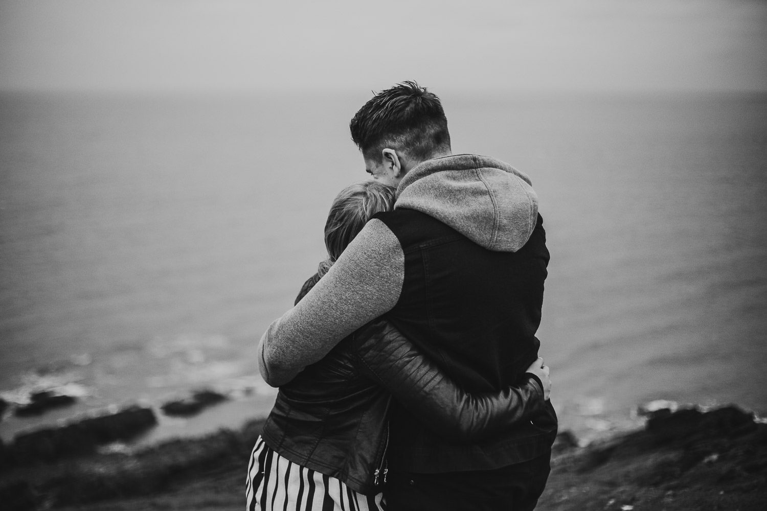 Bride and groom embrace during windy by the sea engagement shoot