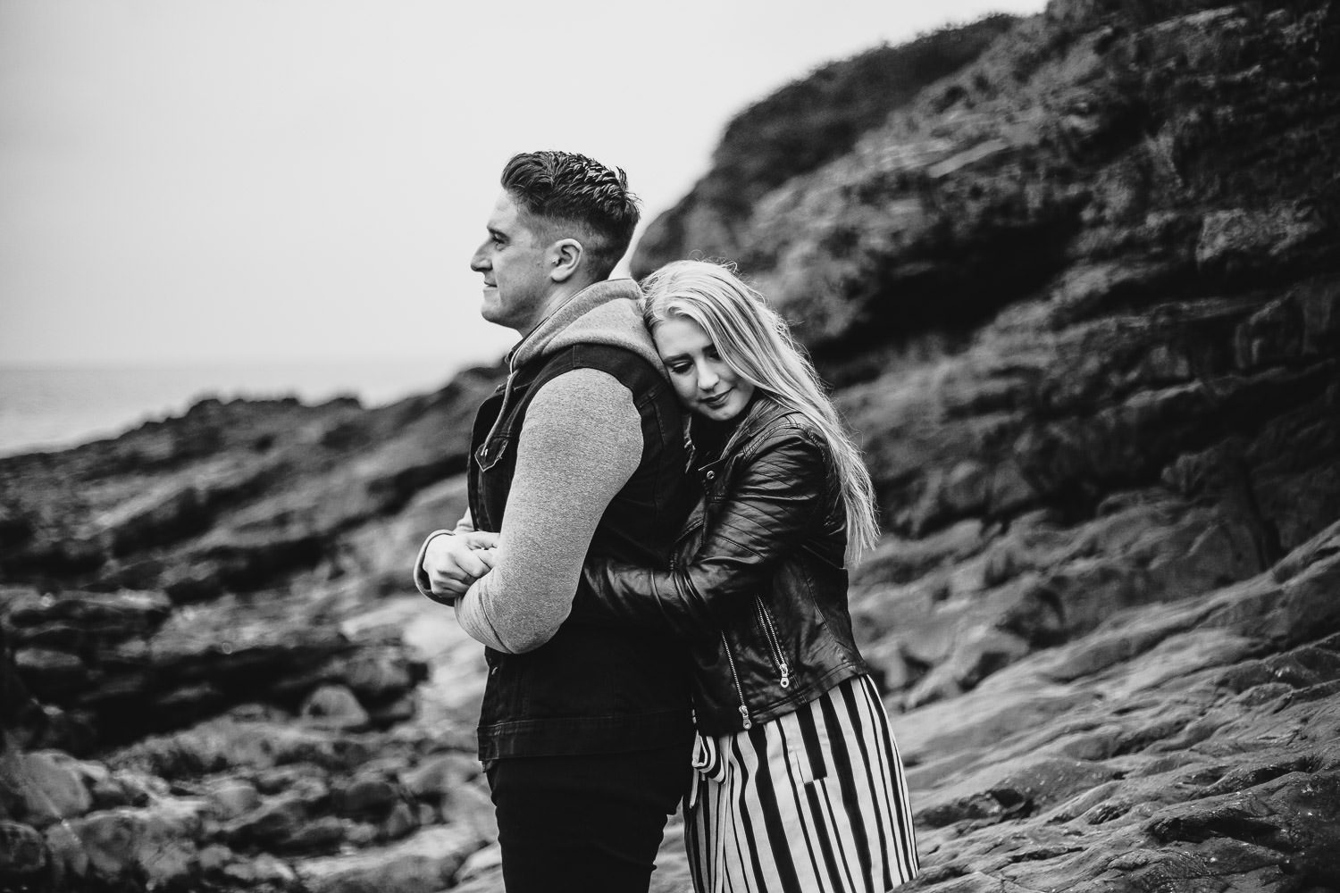 Bride cuddles groom black and white seaside engagement shoot